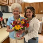 2 females holding a container filled with flowers