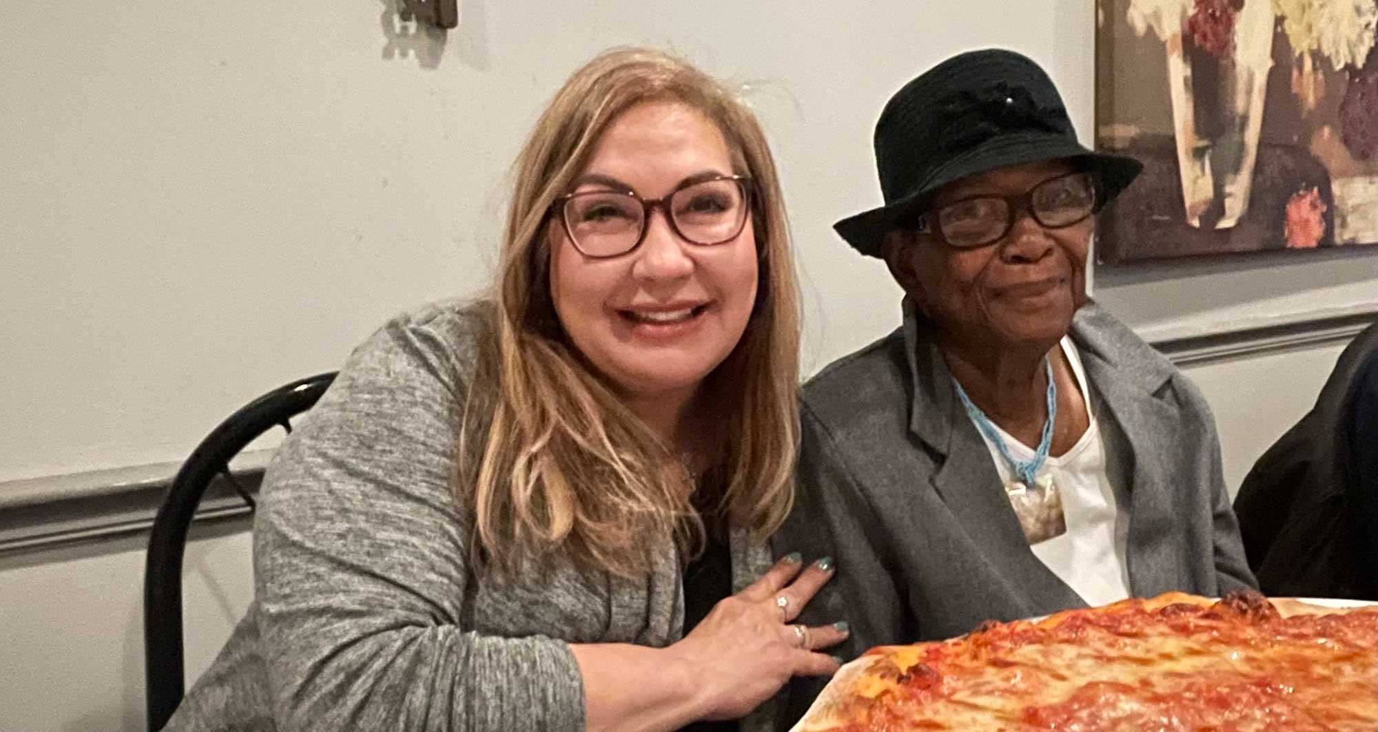 2 female sitting at a table with pizza